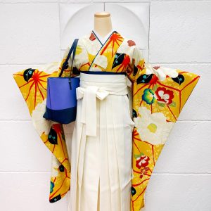 黄色に赤白椿の振袖に白袴の卒業式着物スタイル。バッグは青