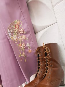 扇の刺繍が入った薄紫の袴と茶色のブーツのアップ画像。花びらを纏う扇は絢爛で綺麗