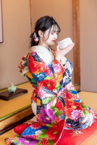 格式ある和空間でスイーツ・お茶を楽しむ白地に椿柄の振袖女性
