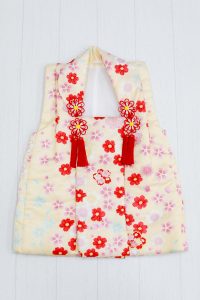 七五三(3歳用)の被布レンタル商品画像。クリーム色に小花、桜の花が描かれた被布。背景はややグレー。