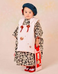 昭和っぽい黒白の小さい桜づくしな女の子七五三 かしいしょう にピンクの生地に鞠の刺繍入り被布コートのアンティークキモノレンタルに青色のベレー帽で レトロモダン に着る千歳飴を持った女児。ショールといったマイセレクトした洋装小物で写真を撮る事も出来る。ブログにはshikibu romanやjillstuartっぽいkimonoも掲載。kimonoだけでなく、足袋、履物、小物、長襦袢。留袖なら袋帯も価格に含まれているので三泊四日で安心