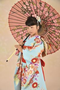 水色に楓のkimonoに赤の帯揚げをしごいた七歳の女の子がﾋﾟﾝｸの傘を持った七五三写真。身長が高いので成人の様にしっかりしている。色あせる事ない美しい和装姿