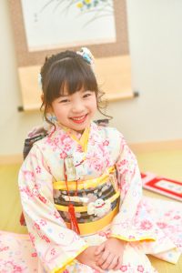 七五三着物レンタル7歳、ポンポネットのレンタル七歳女児用着物。淡いクリーム色や黄色(イエロー・黄)、ピンク、水色、緑色の七五三を祝う晴れ着。ピンクと水色のリボンで流水文様が描かれ、梅・梅花、桜・桜花が描かれる、帯解の儀やお正月の神社参拝などにも着用するジュニア着物。式部浪漫(shikibu roman)や九重、lilli、ciaopanic、紅一点、ﾒｿﾞﾋﾟｱﾉブランドではありません。宅配可