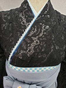 ブラックの総レース生地に、ナカノヒロミチの淡い水色の刺繍入り袴と同じ色の重ね衿を組み合わせた卒業式袴コーデ。帯の市松模様がよく見えるウエストから上の画像