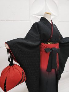 胸元に紅梅の刺繍だけがある、喪服のように真っ黒の無地きもの。赤から黒のぼかし入り袴を着付け た卒業式用の祝い着和装。シンプルかつ個性的。赤い巾着を持っている