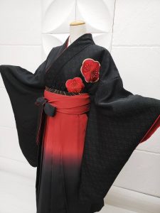 胸元に大きな紅梅の刺繍だけがある、喪服のように真っ黒の無地きもの。赤から黒のぼかし入り袴を着付け た卒業式用の祝い着和装。シンプルかつ個性的。