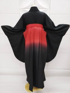 胸元に赤い梅の刺繍だけがある、喪服のように真っ黒の無地きもの。赤から黒のぼかし入り袴を着付け た卒業式用の祝い着和装。シンプルかつ個性的（背中側のフォト）