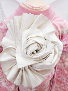 ガーリーな洋服で大人気なリズリサブランドのピンクのバラ柄furisode。白無垢用の袋帯を複雑な薔薇の形に巻いている。帯結びがよく分かる後姿のアップ画像（桃パフェをイメージしてコーディネート）