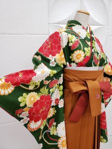 深緑に赤、オレンジ、黄色で牡丹、八重菊、薬玉がプリントされた定番古典柄のレンタルキモノ。hakamaは濃いベージュに鞠のワンポイント刺繍入り。オーソドックスで美しい和のお祝いスタイル