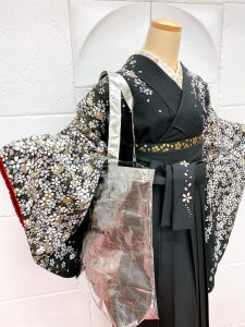 黒地に金銀の小桜がぎっしり描かれた卒業式着物に裾と紐に桜の刺繍が入った黒袴を着付けられたトルソー写真。シンプルかつ綺麗な組み合わせ。シルバーの大きいバッグを提げている