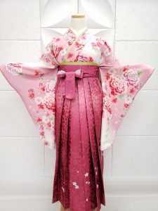 薄ピンクに牡丹の衣装に濃い桃色のぼかし、刺繍、レース入りの袴を着付けている。可愛らしいフルセットレンタルの一例