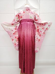 薄ピンクに牡丹の衣装に濃い桃色のぼかし、刺繍、レース入りの袴を着付けている。可愛らしいフルセットレンタルの一例。背中心側