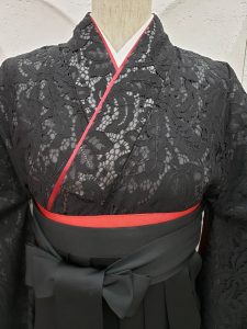 黒の総レースの二尺袖にブラック無地袴、赤の帯を巻いた卒業式袴のワントーンコーディネート。赤い重ね衿やレースの模様がよく見える胸元写真
