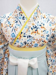 白地に青、水色、ベージュ、オレンジの小花柄小紋きものに、淡い水色の袴の組み合わせ。卒業式袴でおすすめの淡色コーデ。胸元の重ね衿がよく分かる写真