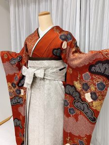 ブラウンに焦げ茶や金で松と梅、流水文様が描かれた総絞り振袖にグレーの袴を着付けた卒業式袴のコーデ写真。ブーツともおすすめ