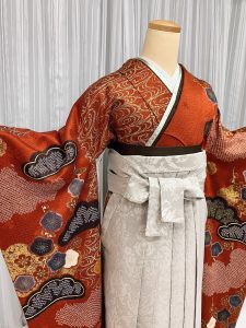 ブラウンに焦げ茶や金で松と梅、流水文様が描かれた総絞り振袖にグレーの袴を着付けた卒業式袴のコーデ写真。ブーツともおすすめ