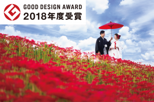 2018年グッドデザイン賞に輝いた彼岸花の結婚式の写真。真っ赤な彼岸花の咲き誇る土手沿いを白無垢と紋付きの新郎新婦が歩いている